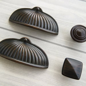 Peut inclure: Trois boutons de porte en bronze antique. Deux sont arqués, avec un motif cannelé, et un est carré.