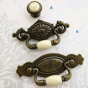 Peut inclure: Un assortiment de quincaillerie d'armoire de style antique. Comprend un bouton rond et deux poignées. La quincaillerie est en métal de couleur bronze avec des accents en céramique crème. Les poignées présentent des motifs floraux ornés.