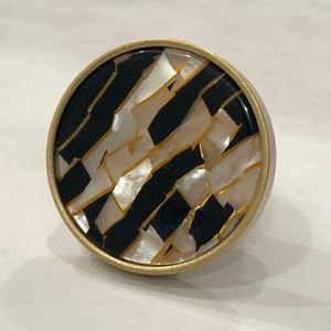 Peut inclure: Un bouton de porte rond en or avec un motif géométrique noir et blanc. Le motif est composé de lignes noires et de pièces blanches en forme de coquille.