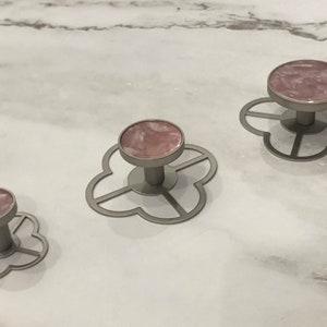 Może przedstawiać: Trzy ozdobne gałki w kolorze różowym i srebrnym z wzorem koniczyny czteroliściennej. Gałki są w różnych rozmiarach.