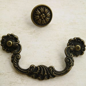May include: A pair of ornate, antique-style cabinet pulls with a decorative floral design. The pulls are made of metal and have a bronze finish.
