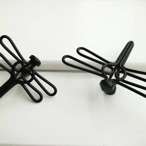 Peut inclure: Deux poignées de tiroir en métal noir en forme de libellule. Les poignées sont en métal fin et présentent un design délicat et complexe.