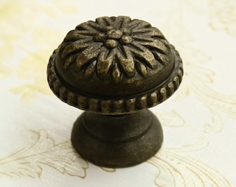 May include: A bronze-colored cabinet knob with a floral design. The knob has a round top and a cylindrical base.