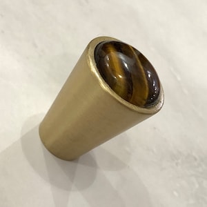 May include: A gold-toned cabinet knob with a round, brown tiger's eye stone inset.