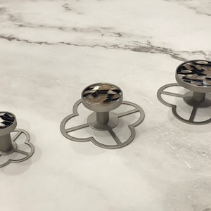 May include: Three silver cabinet knobs with a four-leaf clover design. The knobs have a brown and black patterned top.