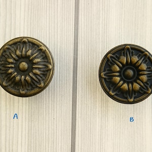 Puede incluir: Dos pomos de armario de latón antiguo con un diseño floral. Los pomos son redondos y tienen un centro elevado con un círculo más pequeño en el medio. Los pomos están etiquetados como A y B.