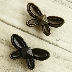 Op de afbeelding: Twee antieke vlinder-ladegrepen met een piramidevormig midden. De grepen zijn van metaal en hebben een donkerbruine afwerking.