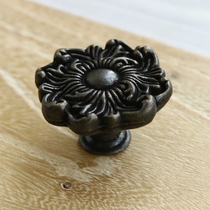 Może przedstawiać: Czarny metalowy gałka do szafki z ozdobnym wzorem kwiatowym.