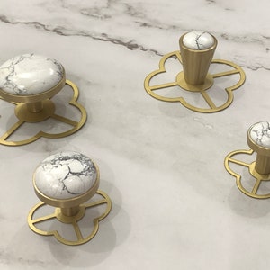 May include: Set of four white marble and brass cabinet knobs with a flower-shaped base. The knobs are different sizes and have a white marble top with black veining.