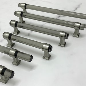 Könnte beinhalten: Ein Satz aus sechs klaren Glas-Schrankgriffen mit gebürstetem Nickel-Finish. Die Griffe sind in verschiedenen Längen erhältlich.