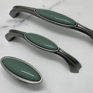 May include: Three cabinet pulls with a silver finish and a light green oval ceramic insert. The pulls are in different sizes.