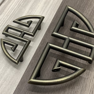 May include: Two antique-style, black metal cabinet pulls with a geometric design. The pulls are shaped like a half-circle and have a raised, intricate pattern.