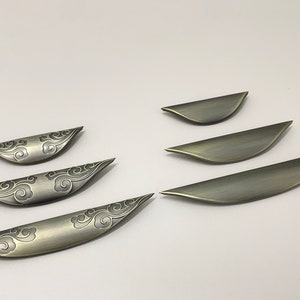 May include: Five antique gold cabinet pulls with a cloud design. The pulls are different sizes and are arranged in a row.