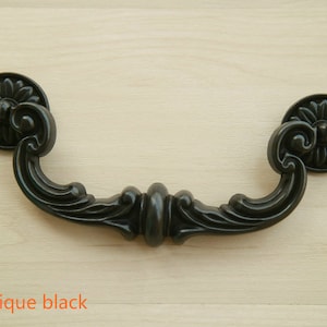 Puede incluir: Tirador de armario negro antiguo con un diseño floral decorativo. El tirador tiene una forma curva y está hecho de metal.