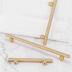 Könnte beinhalten: Drei goldene Schrankgriffe mit abgerundeten Enden. Die Griffe haben unterschiedliche Längen.