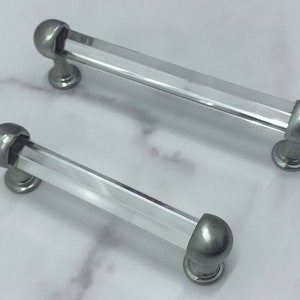 Puede incluir: Dos pomos de armario de vidrio transparente y plateado con forma redonda ligeramente abovedada. Los pomos tienen un centro de vidrio transparente y una base de metal plateado.