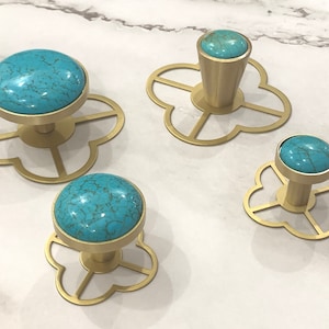 May include: Four gold-toned cabinet knobs with turquoise stone inlays. Each knob is mounted on a decorative four-leaf clover-shaped base.