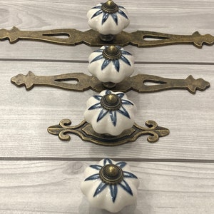 Pode incluir: Três botões de armário de cerâmica branca com um design floral azul e placas de base de latão antigo.