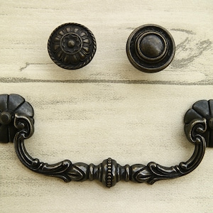 May include: A set of three antique-style cabinet knobs and a pull handle. The knobs are round with a floral design and the pull handle is ornate with a floral design.
