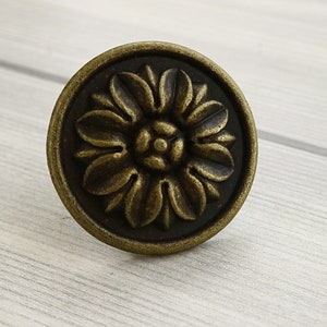 Könnte beinhalten: Ein runder, antiker Messing-Schrankknauf mit einem dekorativen Blumenmuster.