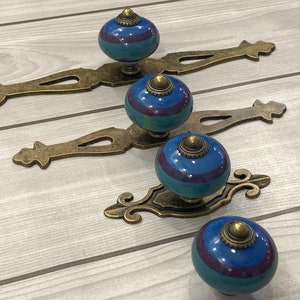 May include: Four antique-style cabinet knobs with ornate metal bases and blue and purple striped ceramic tops.