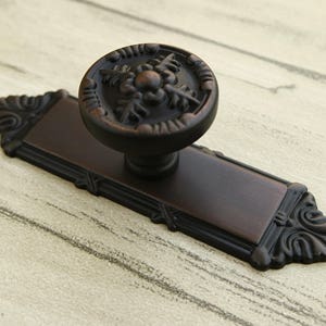 Peut inclure: Un bouton de porte en bronze avec un motif floral décoratif et une plaque arrière rectangulaire assortie.