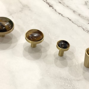 May include: Four gold-toned cabinet knobs with tiger's eye stone inlays. The knobs are round and have a smooth, polished finish.
