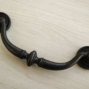 May include: A black metal drawer pull with a curved handle and a decorative knob in the center.