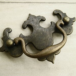 Peut inclure: Tiroir en laiton antique avec un design décoratif et orné. La poignée a une poignée en boucle et une finition vieillie.