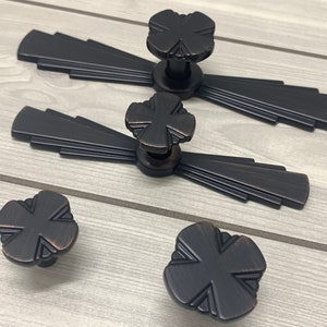 May include: Four black metal cabinet knobs with a geometric design. Two knobs are attached to decorative plates with a fan-shaped design.