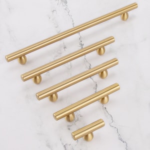 May include: Five gold-toned cabinet pulls with rounded ends. The pulls are arranged in a descending size order, with the largest pull at the top and the smallest pull at the bottom.