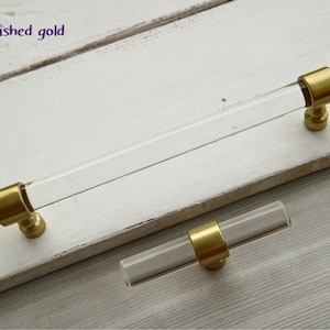 May include: Two brushed gold cabinet pulls with clear acrylic rods. The larger pull is approximately 15 cm long and the smaller pull is approximately 7.5 cm long.