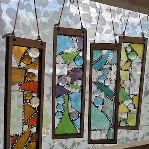 May include: Four rectangular stained glass panels with geometric designs in shades of blue, green, yellow, and orange. The panels are framed in wood and hung on a wall with twine.