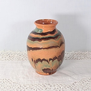May include: A ceramic vase with a rounded body and a flared rim, featuring a marbled glaze pattern in shades of terracotta orange, dark brown, and sage green. The surface has a smooth, glossy finish with horizontal bands of color throughout.