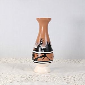 May include: A brown ceramic vase with a white base and black and white geometric designs. The vase has a rounded body and a narrow neck.
