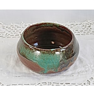May include: A small, round ceramic bowl with a brown and green glaze. The bowl has a rustic, handmade look.