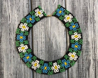 Könnte beinhalten: Eine Perlenkette mit Blumenmuster. Die Kette besteht aus schwarzen, weißen, blauen und grünen Perlen. Die Perlen sind in einem Blumenmuster angeordnet.