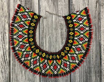 May include: A black beaded necklace with a geometric pattern in red, yellow, green, and white. The necklace has a fringe of beads around the bottom.