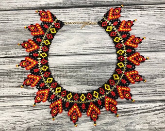 Peut inclure: Un collier de perles noires, rouges et jaunes avec un motif géométrique. Le collier est fait de petites perles et présente un design délicat et complexe.