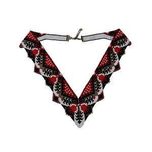 Puede incluir: Un collar de cuentas rojas, negras y blancas con un diseño en forma de V. El collar tiene un borde festoneado y un cierre de broche.