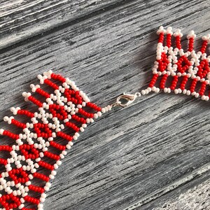 May include: A red and white beaded necklace with a silver clasp. The necklace is made of small, round beads that are arranged in a geometric pattern.