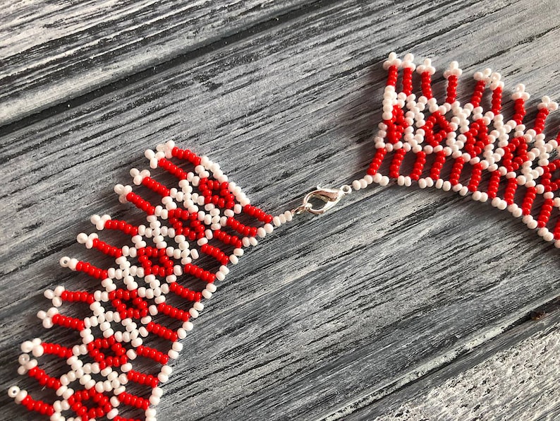 May include: A red and white beaded necklace with a silver clasp. The necklace is made of small, round beads that are arranged in a geometric pattern.