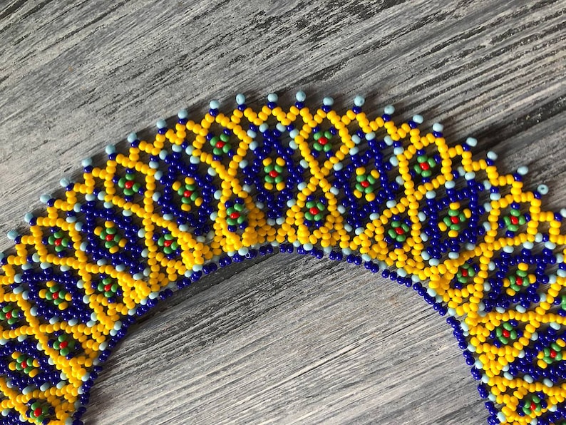 Pode incluir: Um close-up de um colar de contas com um padr&atilde;o geom&eacute;trico em amarelo, azul, verde e vermelho. O colar &eacute; feito de pequenas contas redondas que s&atilde;o enfiadas em um padr&atilde;o repetitivo.