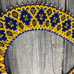 Pode incluir: Um colar de contas com um padr&atilde;o geom&eacute;trico em tons de amarelo, azul e verde. O colar &eacute; feito de contas pequenas e redondas e tem um design delicado e intrincado.