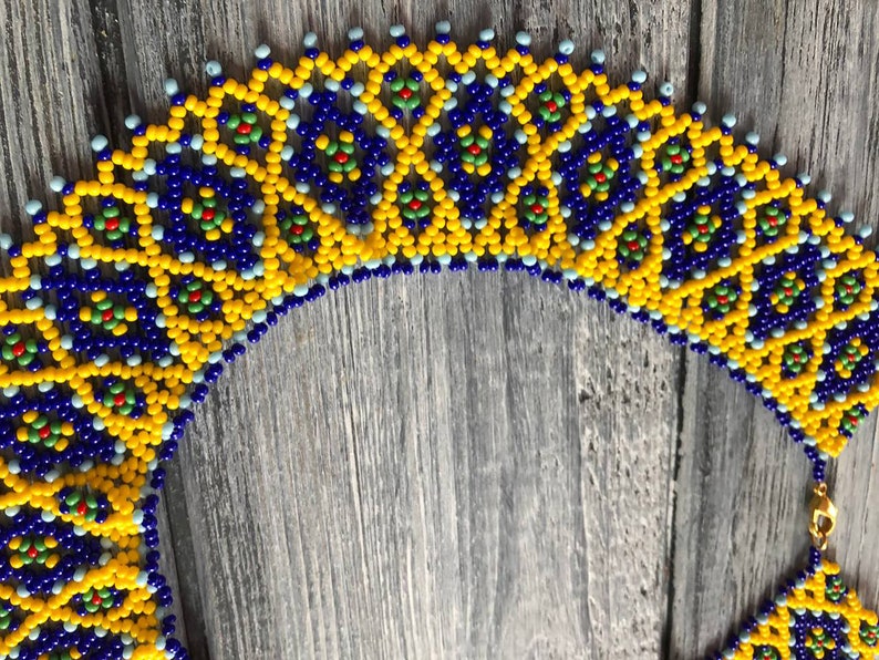 Pode incluir: Um colar de contas com um padr&atilde;o geom&eacute;trico em tons de amarelo, azul e verde. O colar &eacute; feito de contas pequenas e redondas e tem um design delicado e intrincado.