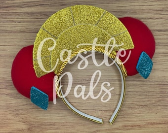 May include: A decorative headband with a gold glitter fan-shaped accent, red circular accents, and blue diamond-shaped accents. The headband has the text "Castle Pals" in white script.