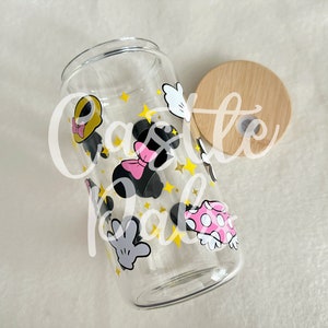 Pode incluir: Uma garrafa de água de vidro transparente com uma tampa de bambu. A garrafa é decorada com um padrão de personagens do Mickey Mouse e Minnie Mouse, estrelas e mãos.