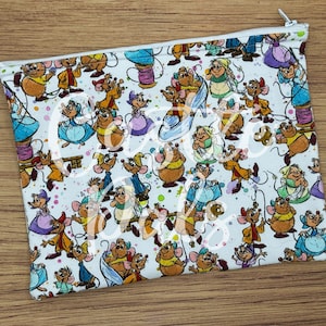 Könnte beinhalten: Eine weiße Reißverschlusstasche mit einem sich wiederholenden Muster von Cartoon-Mäusen in verschiedenen Outfits. Die Mäuse sind in Braun-, Blau-, Gelb- und Lilatönen gehalten. Die Tasche hat einen silbernen Reißverschluss und ist auf einem Holzgrund platziert.