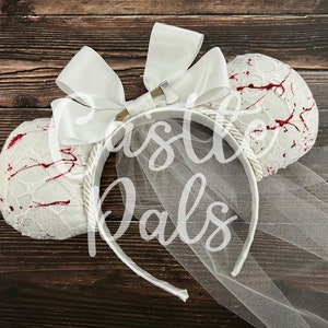 May include: White bridal mouse ears with a white satin bow and a small axe charm. The ears are covered in white lace with red blood splatter and a white tulle veil.