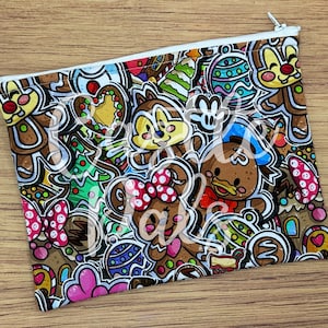 Peut inclure: Une pochette rectangulaire zippée avec un motif de pain d'épices de dessin animé coloré. Le motif comprend des personnages en pain d'épices, des arbres de Noël et des éléments festifs en marron, rouge, vert et bleu. La pochette a une fermeture éclair blanche.